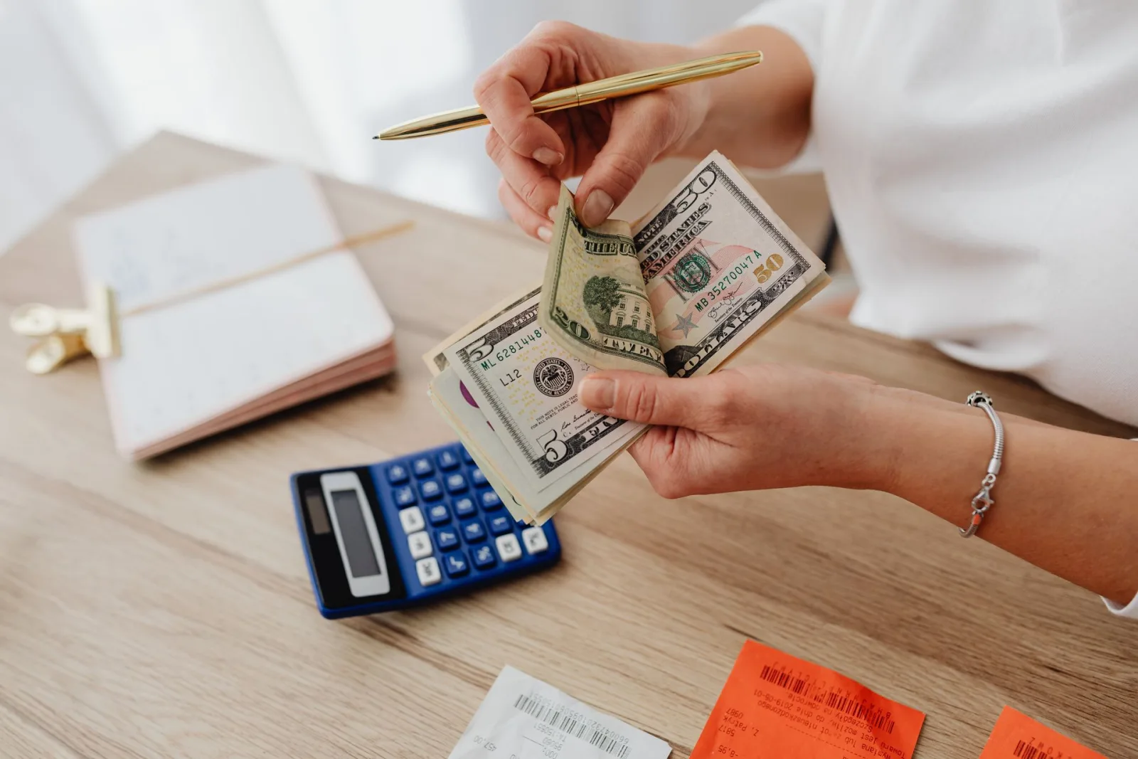 Hands counting cash beside a calculator and notes